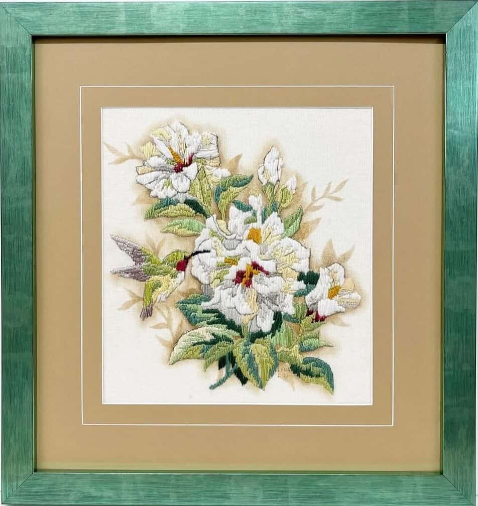 A framed cross stitch of flowers in a green frame.