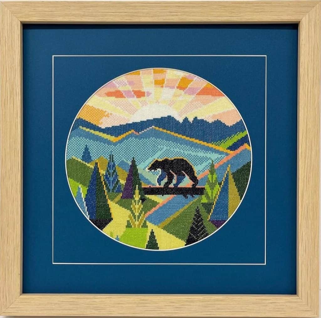 A framed cross stitch of a bear in the mountains.
