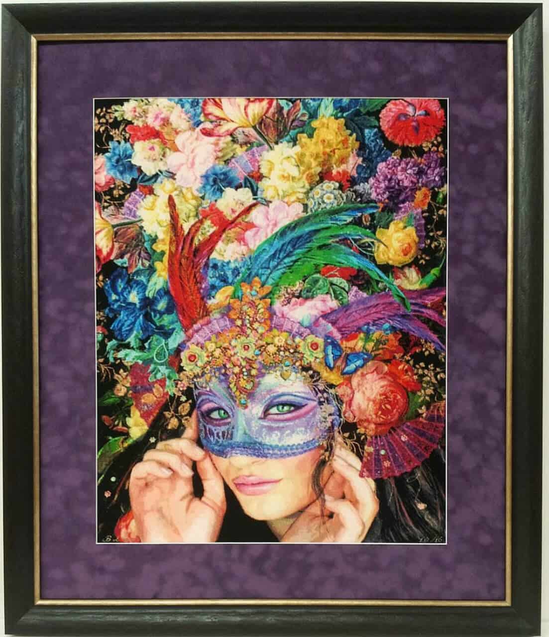 A framed cross-stitch of a woman wearing a colorful mask.