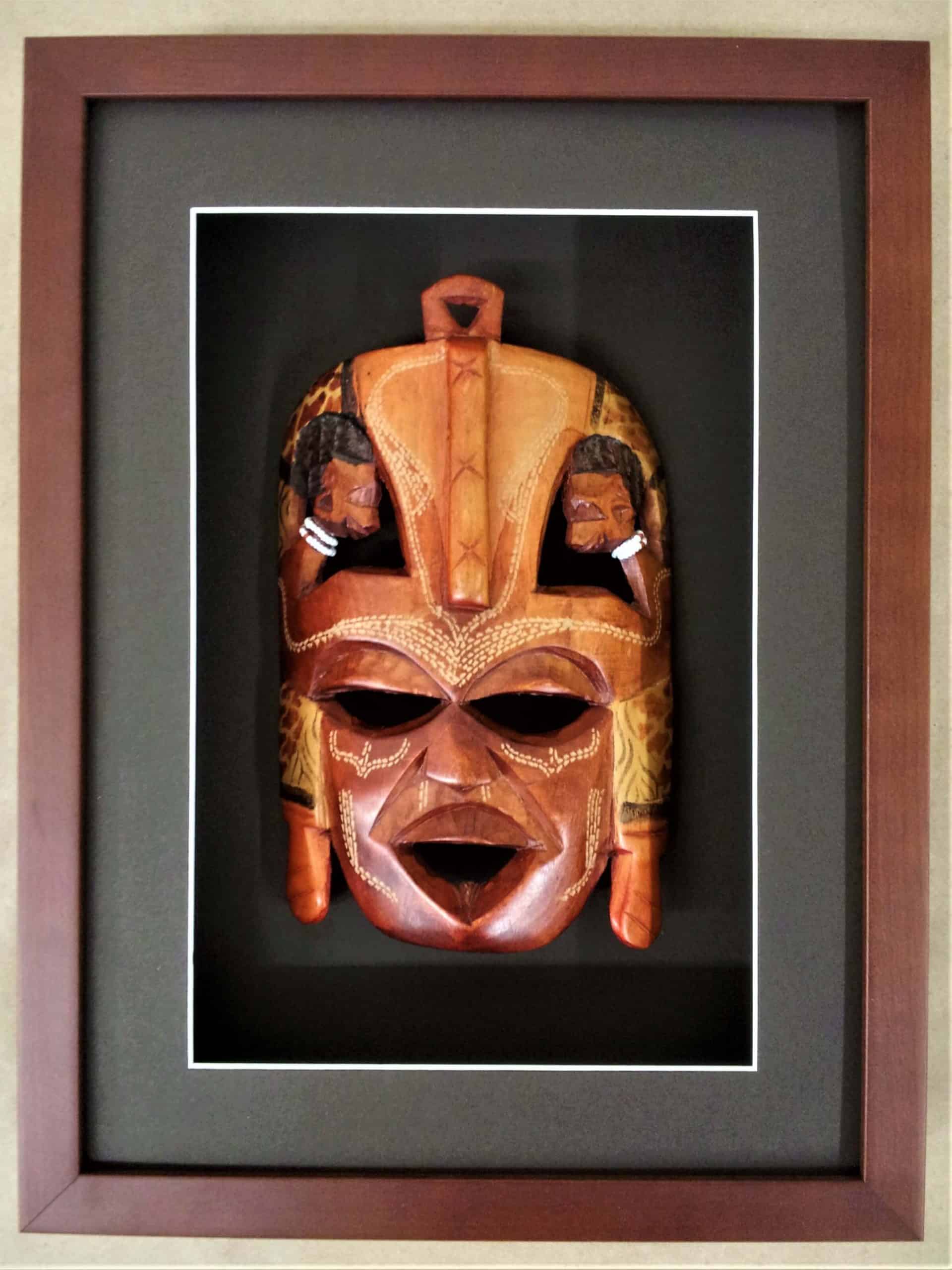 A wooden mask is framed in a wooden frame.