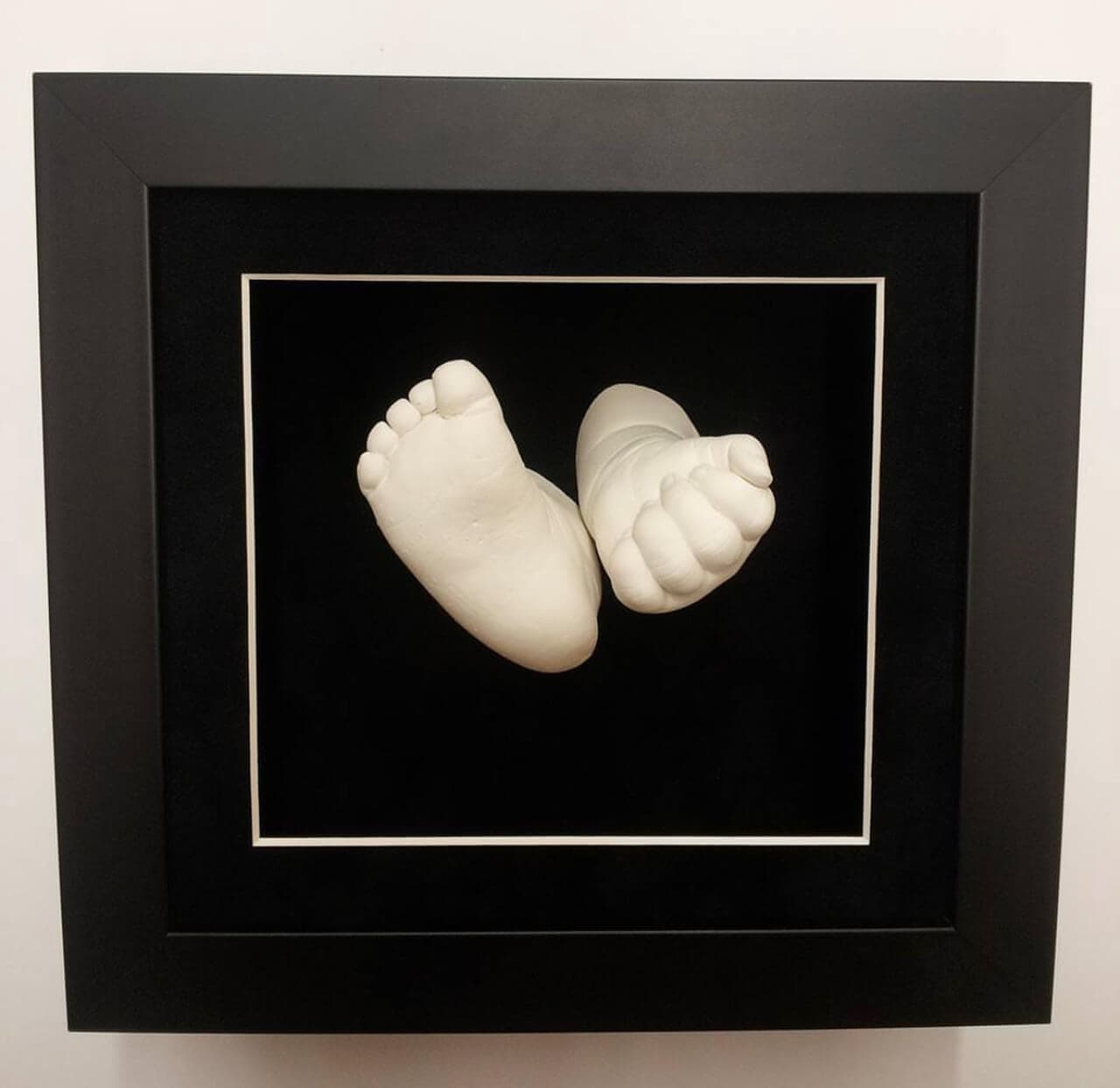 A sculpture of a baby's foot & hand in a black frame.