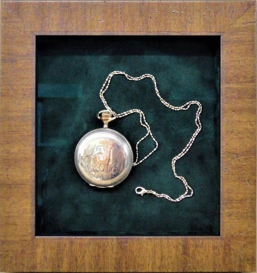 A silver pocket watch in a wooden frame.